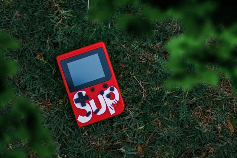 Red retro game console placed on green grass, providing a nostalgic gaming vibe outdoors.